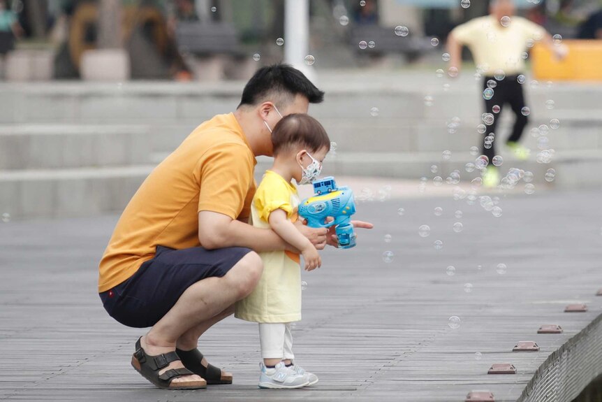 A child wearing a face mask plays with a bubble-making toy at a park