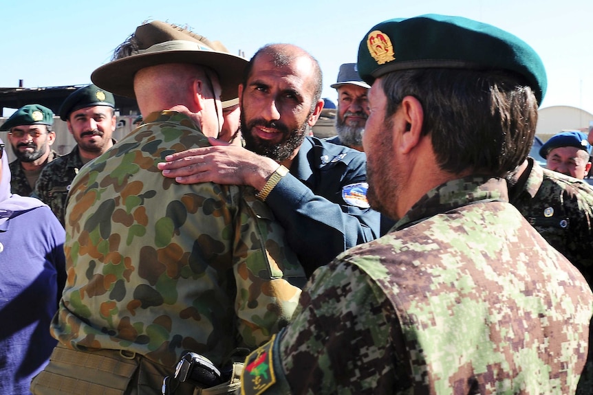 A man in a navy unicorm hugs an Australian soldier in camouflague.
