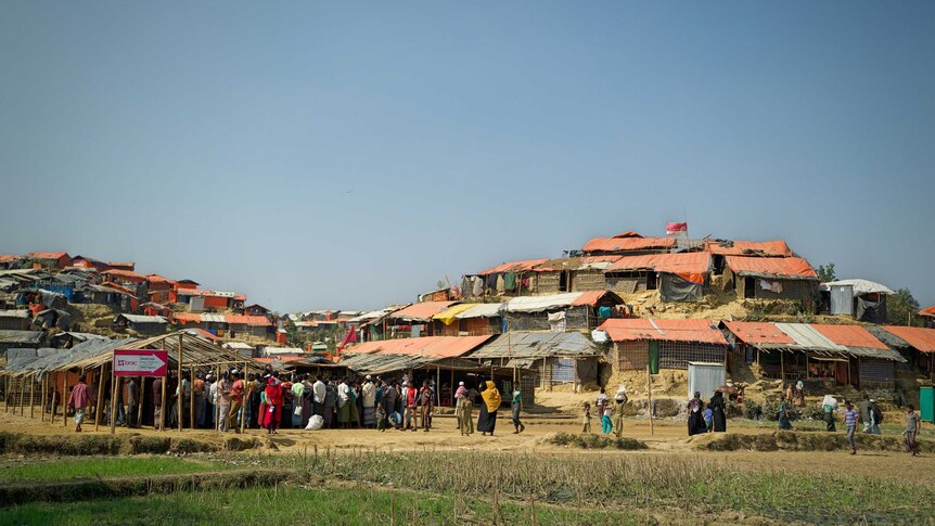 People are seen standing in the Rohingya refugee camp, filled with small shanties.