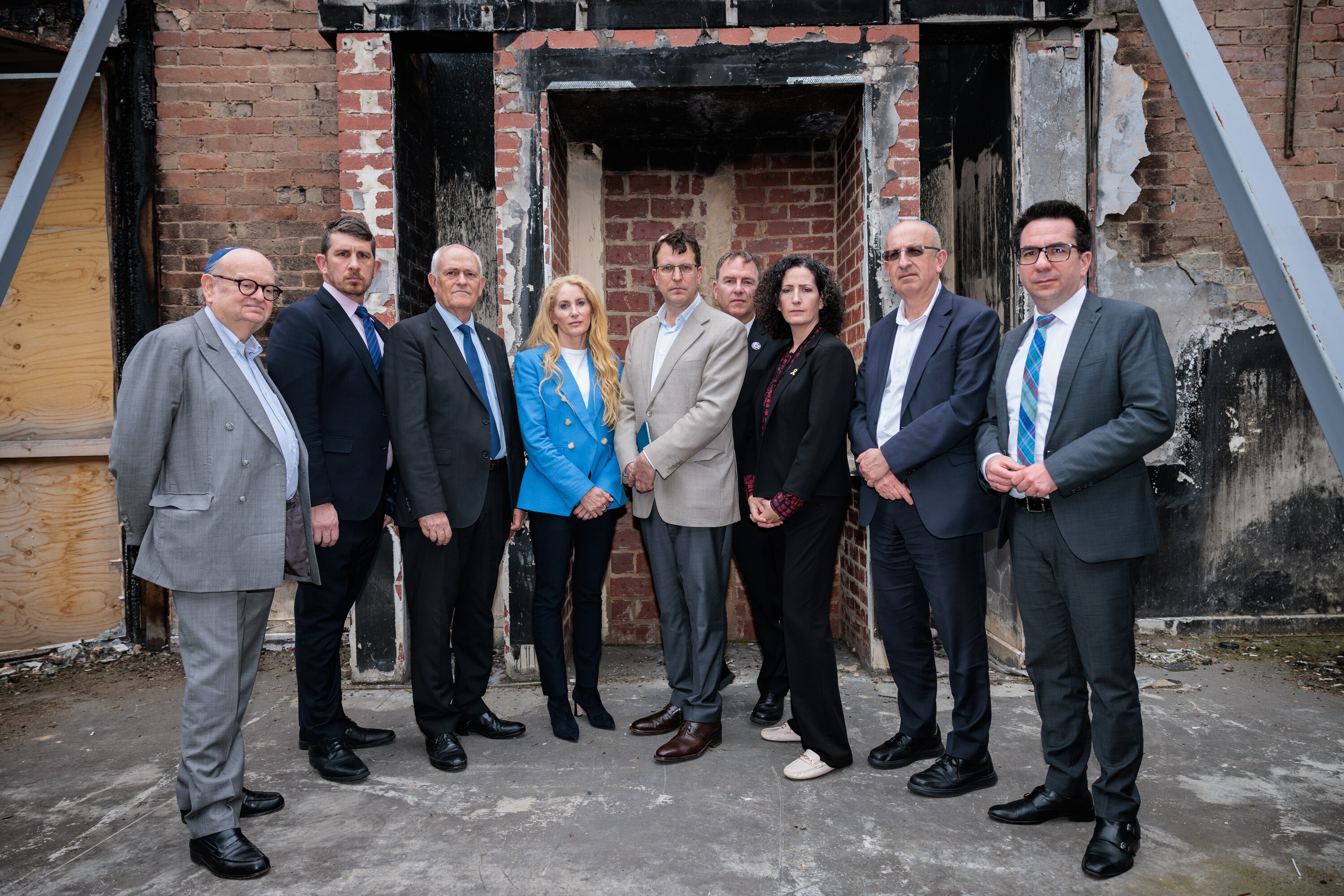 Un grupo de hombres y mujeres vestidos formalmente se encuentran en un edificio incendiado.