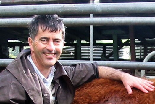 Livestock veterinarian Dr David Rendell stands in a cattle yard, resting his arm on a cow.