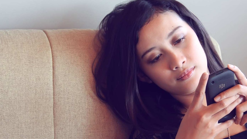 Young woman sitting on a beige couch looking at her phone and appearing lonely