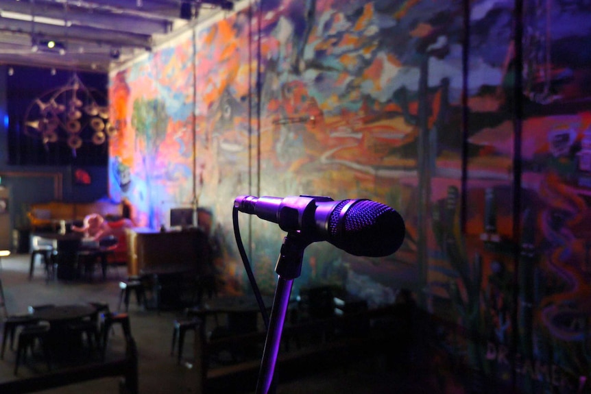 An empty venue with tables and chairs behind a microphone on a stage.