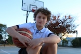Indi Serafin holding a basketball on a basketball court at his high school.