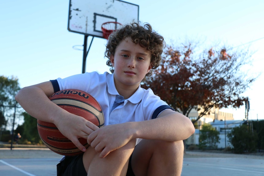 Indi Serafin holding a basketball on a basketball court at his high school.