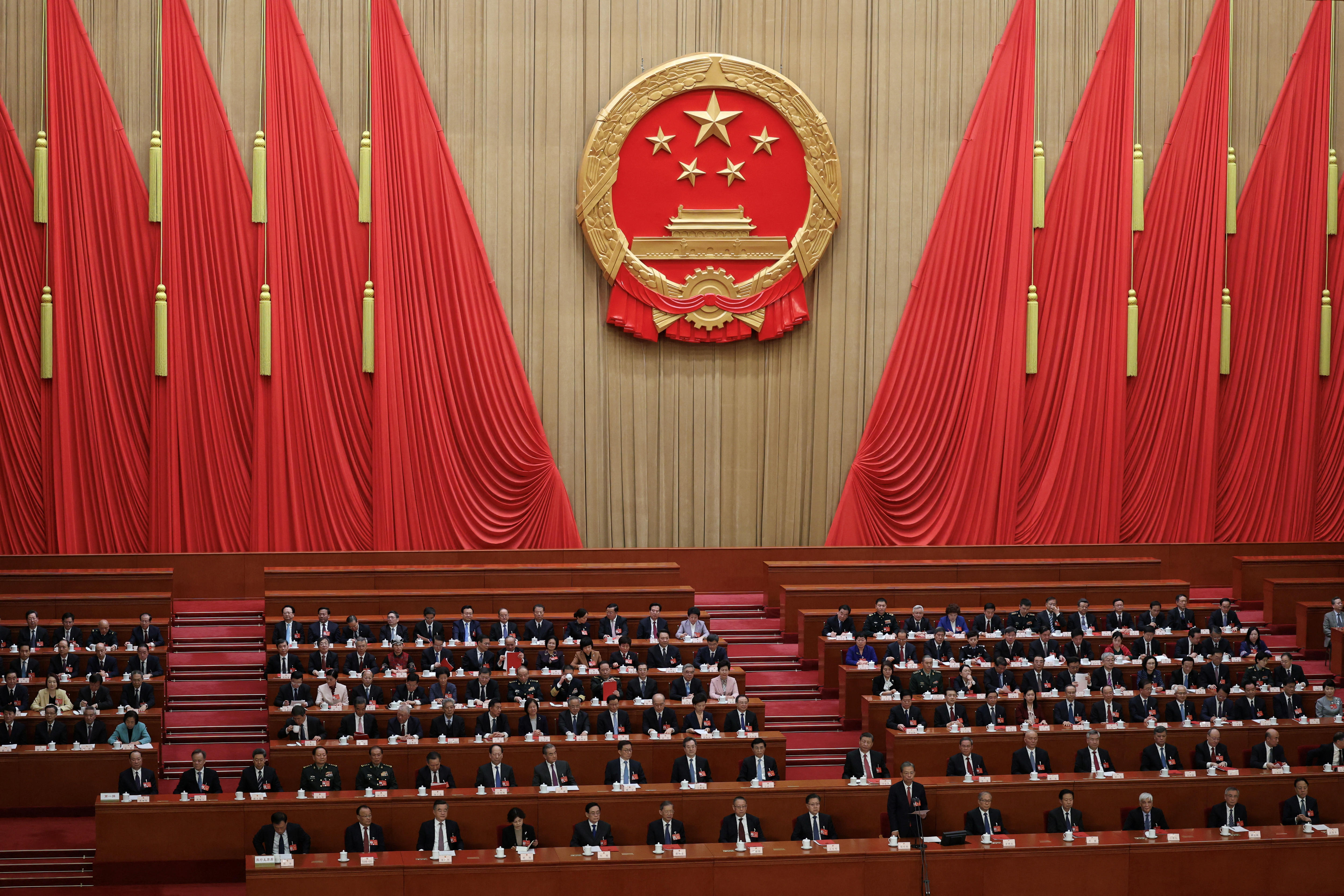 Suited delegates sit in benches in the huge red and gold Great Hall of the People for a meeting of the CCP leadership.