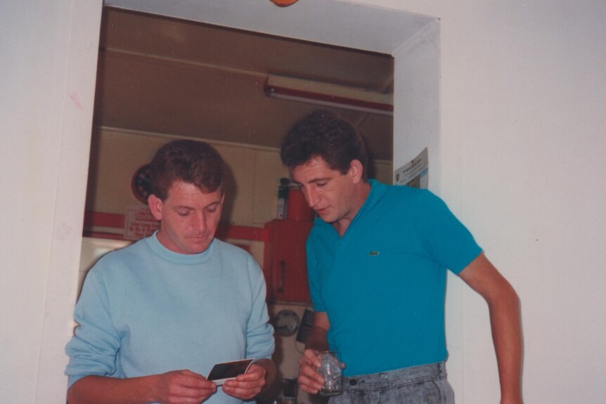 John and Peter Russell are both wearing blue shirts as they look at a polaroid photograph in 1988