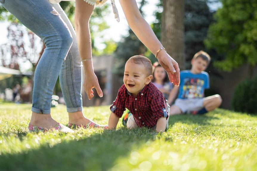 A toddler crawling into his mother's arms while his siblings watch