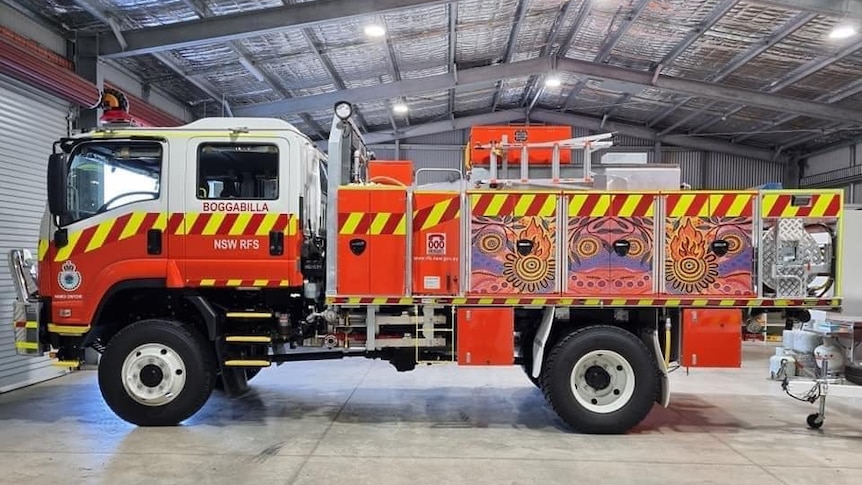 A fire truck painted with an Indigenous design sits at rest in a hangar-like building.