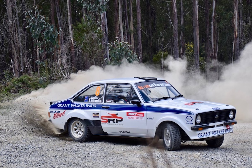 A rally car kicks up a cloud of dust with some trees in the background