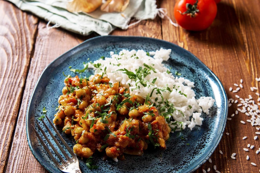 Chickpea curry and white rice on a blue plate on a table to depict the use of ghee in cooking curry.