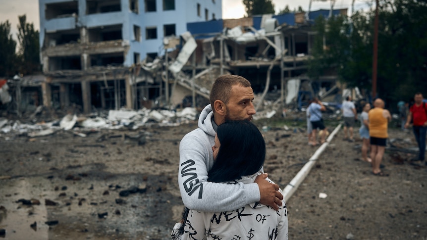 A man and woman stand outside a bomb damaged building in Mykolaiv