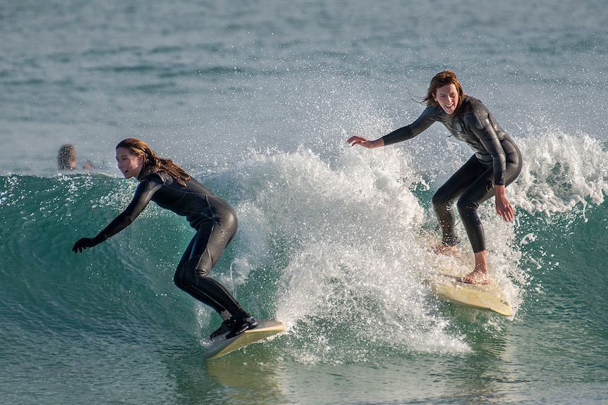 Two women surfing a wave side-by-side. 