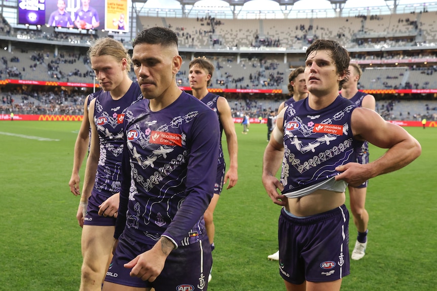 Three Fremantle dockers players, Michael Walters, Hayden Young and Lachie Schultz looking dejected while walking off the field.