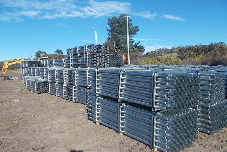 Bundles of steel pipes on farmland with a tractor digger visible in the background.