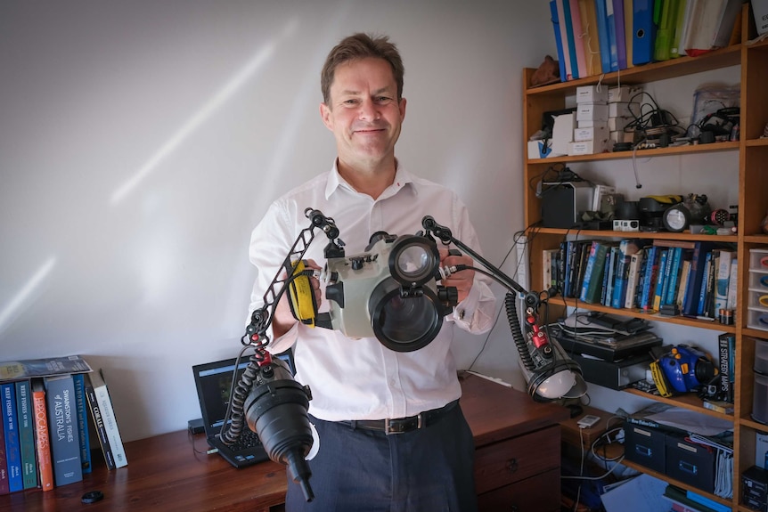 John Sear smiling at the camera, holding his underwater camera.