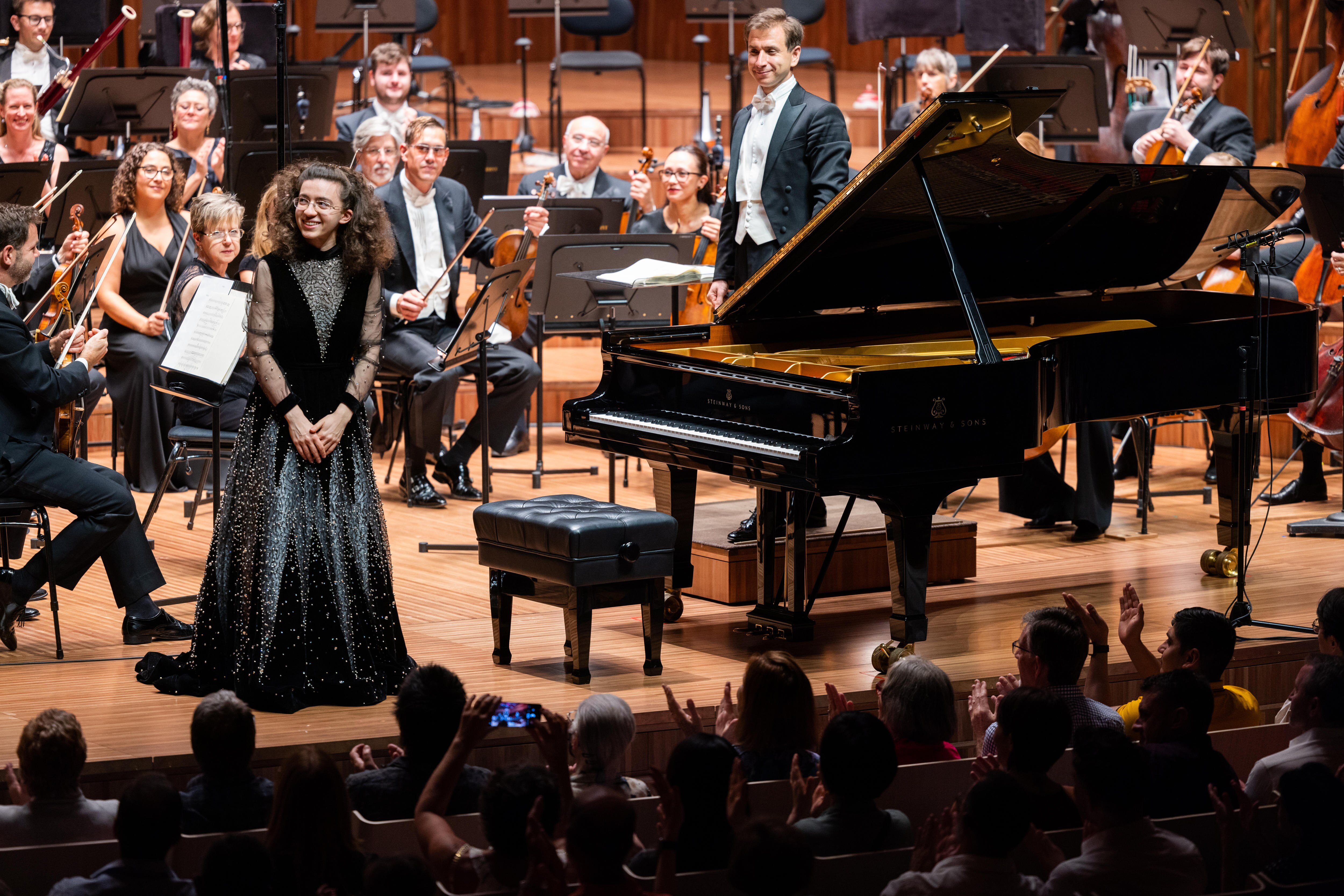 PIanist Marie-Ange Nguci standing in front of the Sydney Symphony Orchestra wearing a resplendent wizard-like dress