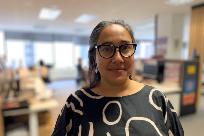 Meena Singh stands in an office and looks into the camera.