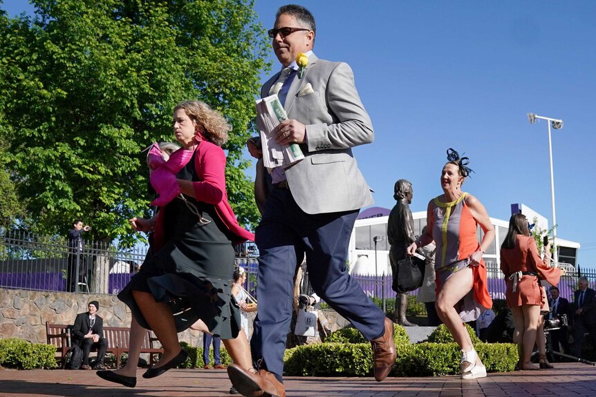 Three people run from the barriers to the track at Flemington Racecourse on cup day.