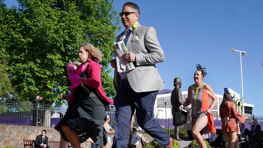 Three people run from the barriers to the track at Flemington Racecourse on cup day.
