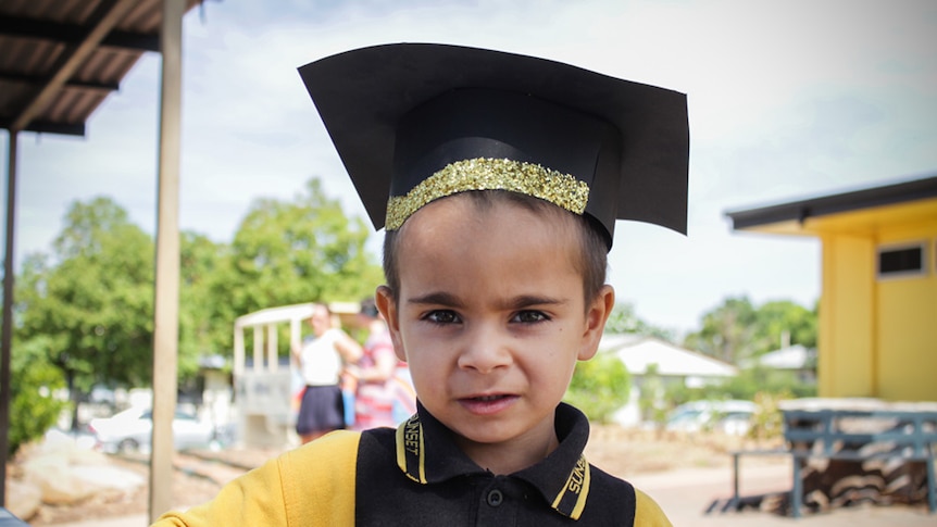 Five-year-old Thomas stares into the camera, dressed in his yellow school uniform and square graduation cap.