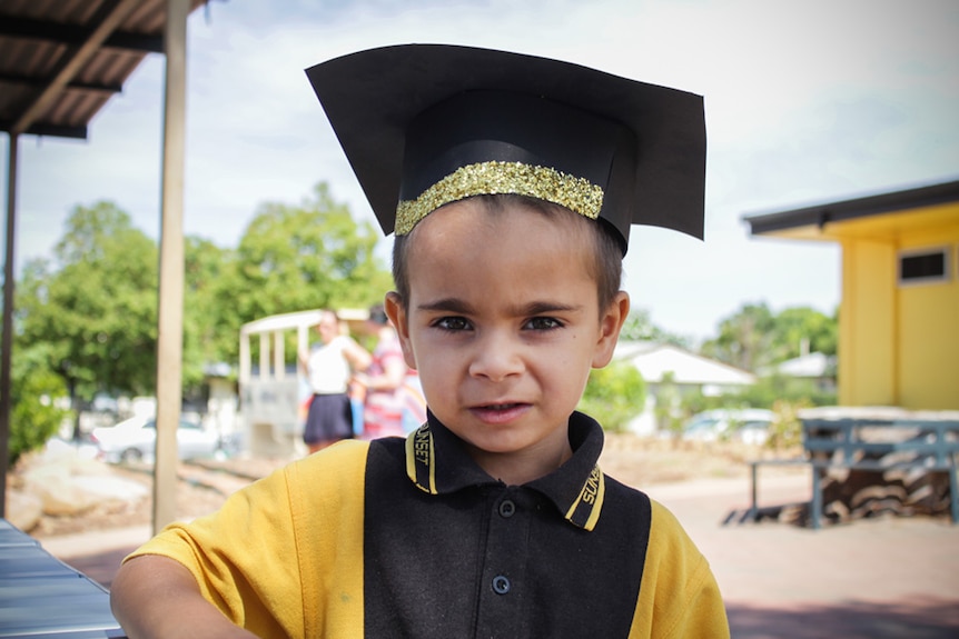 Five-year-old Thomas stares into the camera, dressed in his yellow school uniform and square graduation cap.