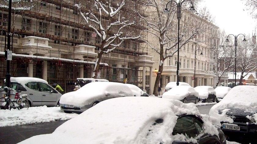 A thick blanket of snow covers cars parked in a London street