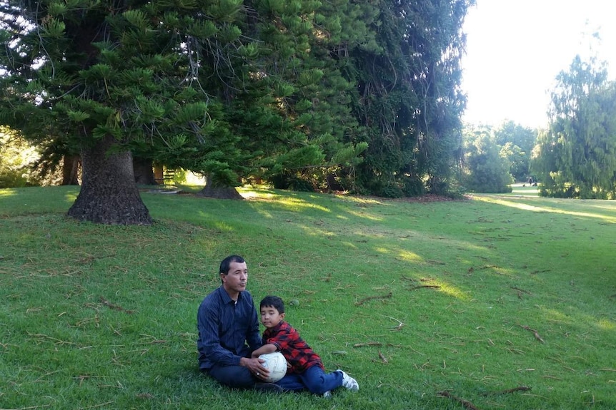 Murtaza Hussain sits next to his father on grass holding a white soccer ball