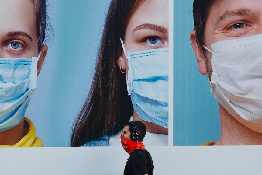 A man wearing an improvised face mask walks by a billboard raising the awareness of wearing face masks in Israel.