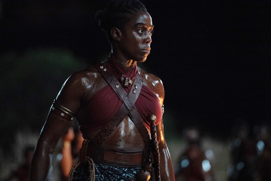 Black woman in red top and brown leather battle gear and knife in her waist looking ready for battle. 