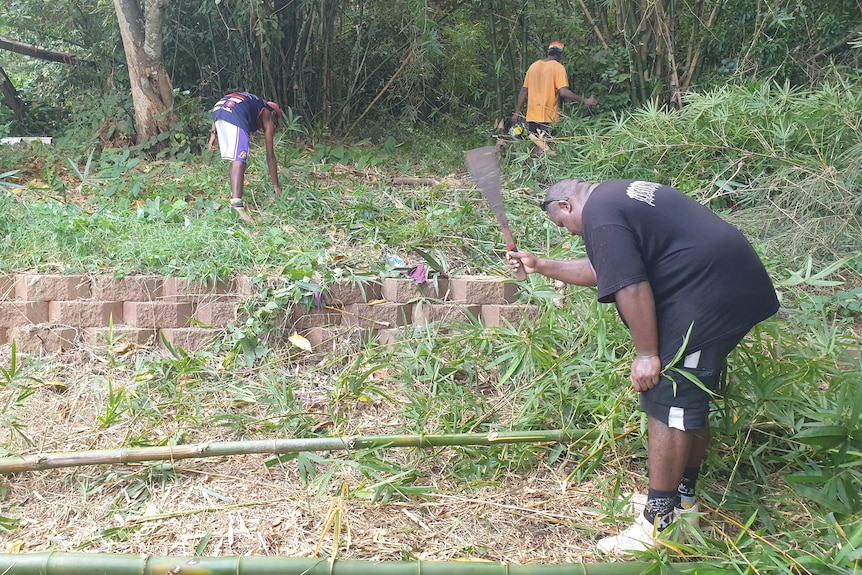 Three men clearing grassland, one holding machete.