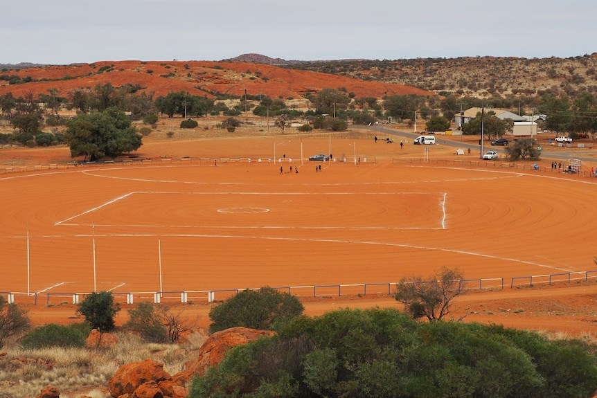 gambar lanskap oval sepak bola tanah oranye dengan pemain di tanah dan bukit di latar belakang