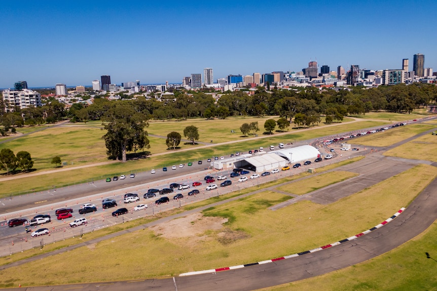 An aerial photo of cars lining up in two rows behind two white tents. In the background is a city skyline