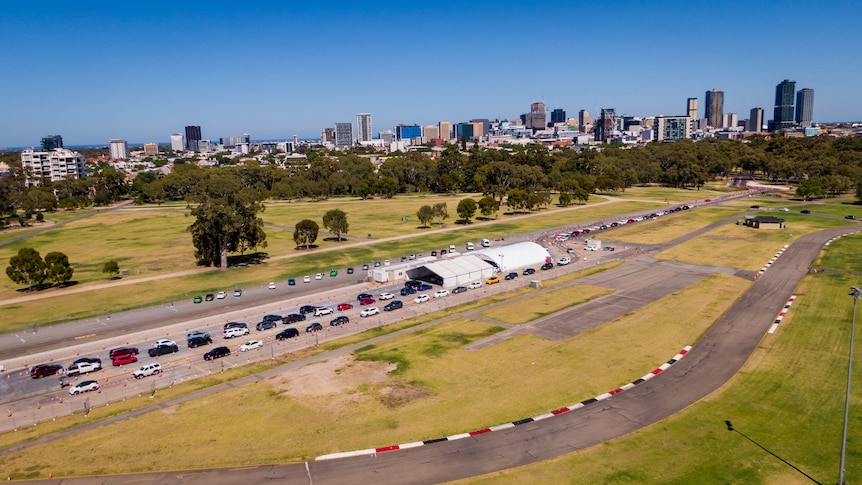 An aerial photo of cars lining up in two rows behind two white tents. In the background is a city skyline