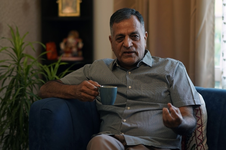 A close up of a man sitting on a couch and holding a tea.