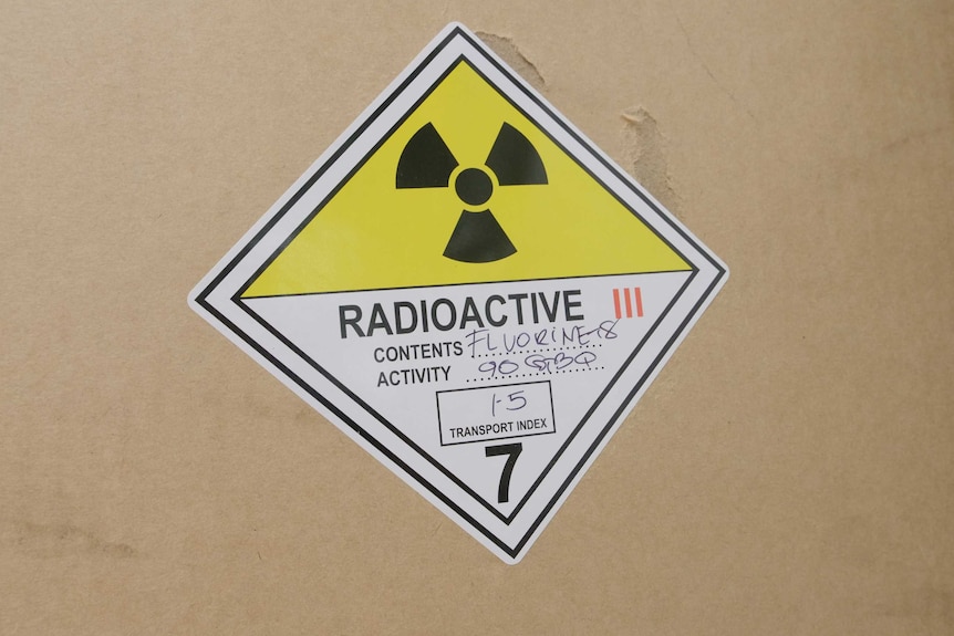 A brown cardboard box with a sticker on the front reading 'radioactive contents: Fluorine18'.