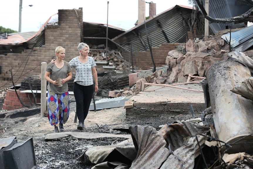 Ingrid Mitchell and Deborah Naif walk through house remnants