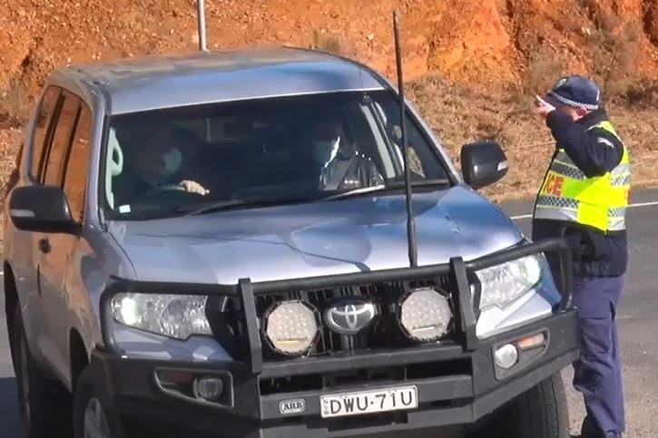 A police officer in high-vis speaks to two others in an unmarked 4WD on a country road.