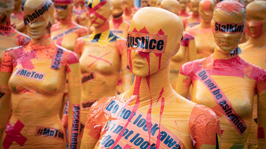 female bodied manniquins taped in plastic with protest signage including "do not look away"