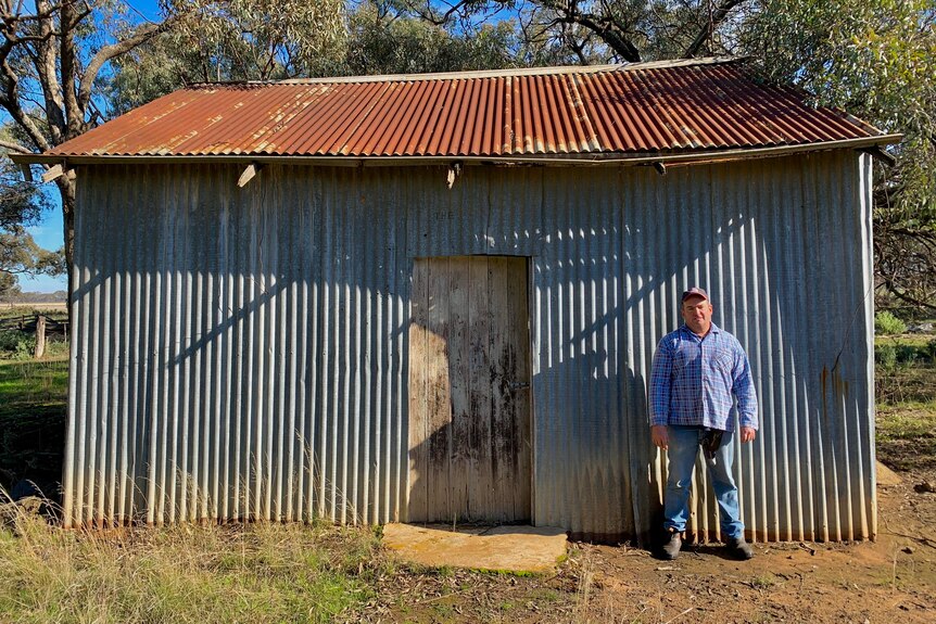 A man is standing in front of an iron barn