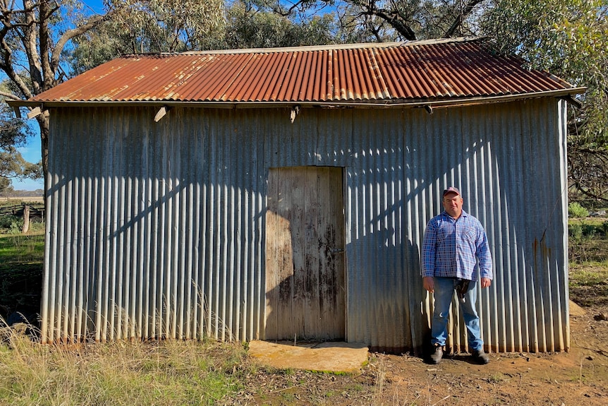 A man is standing in front of an iron barn