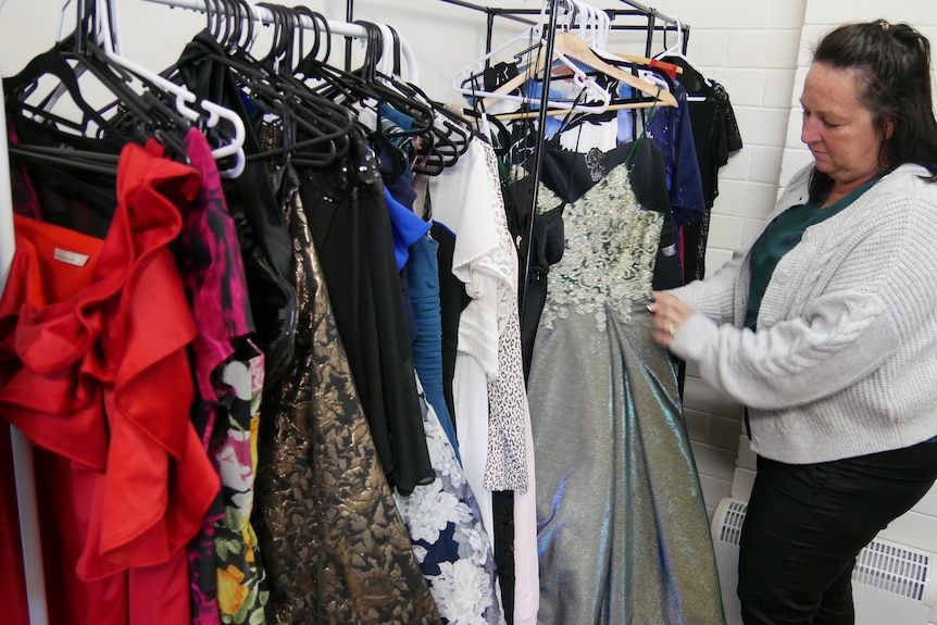 A woman standing next to dresses on coat hangers ahead of school ball.  
