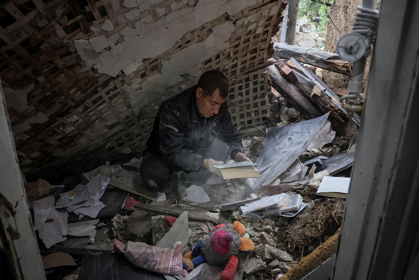 A local resident searches through a pile of belongings as he sits on the floor of his destroyed house.