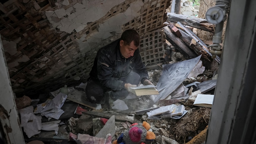 A local resident searches through a pile of belongings as he sits on the floor of his destroyed house.