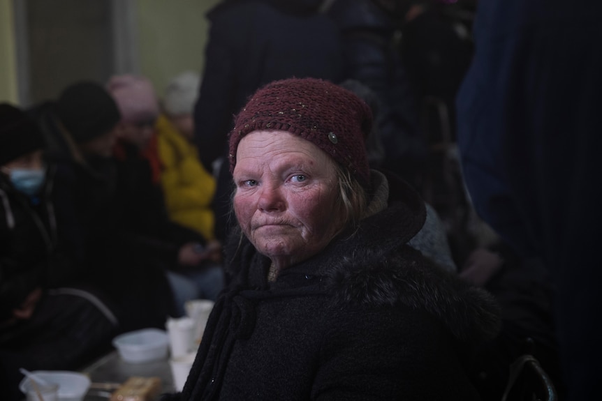 a close up of an older woman in a beanie with dirty red cheeks