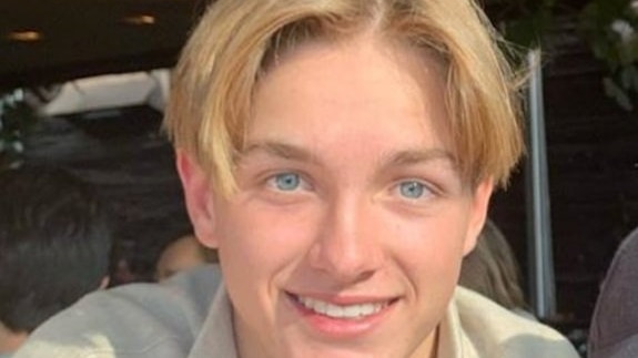 A teenage boy with blonde hair and blue eyes smiling at the camera.