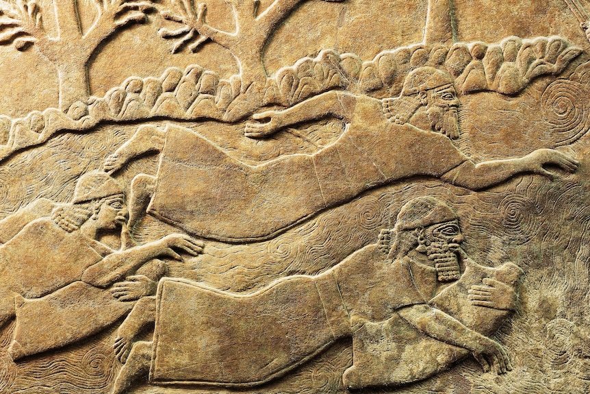 An ancient carving of three people swimming, two of whom are blowing into large bags