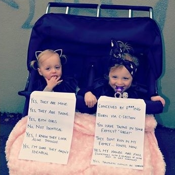 Twin girls in a pram holding signs