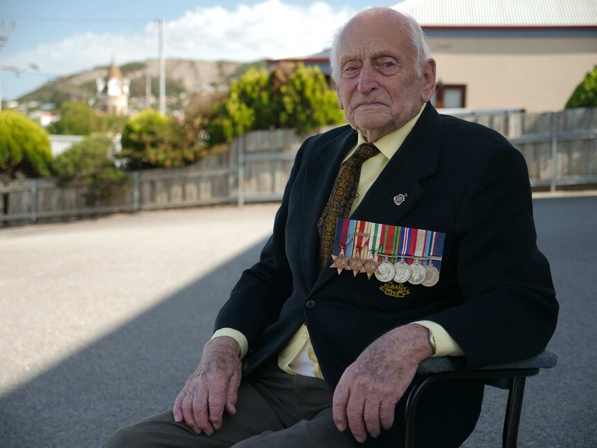 War veteran Evan Hobely, wearing his medals, sits in a chair.