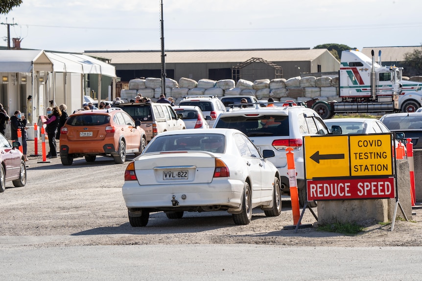 Cars waiting on gravel with a sign saying COVID TESTING STATION